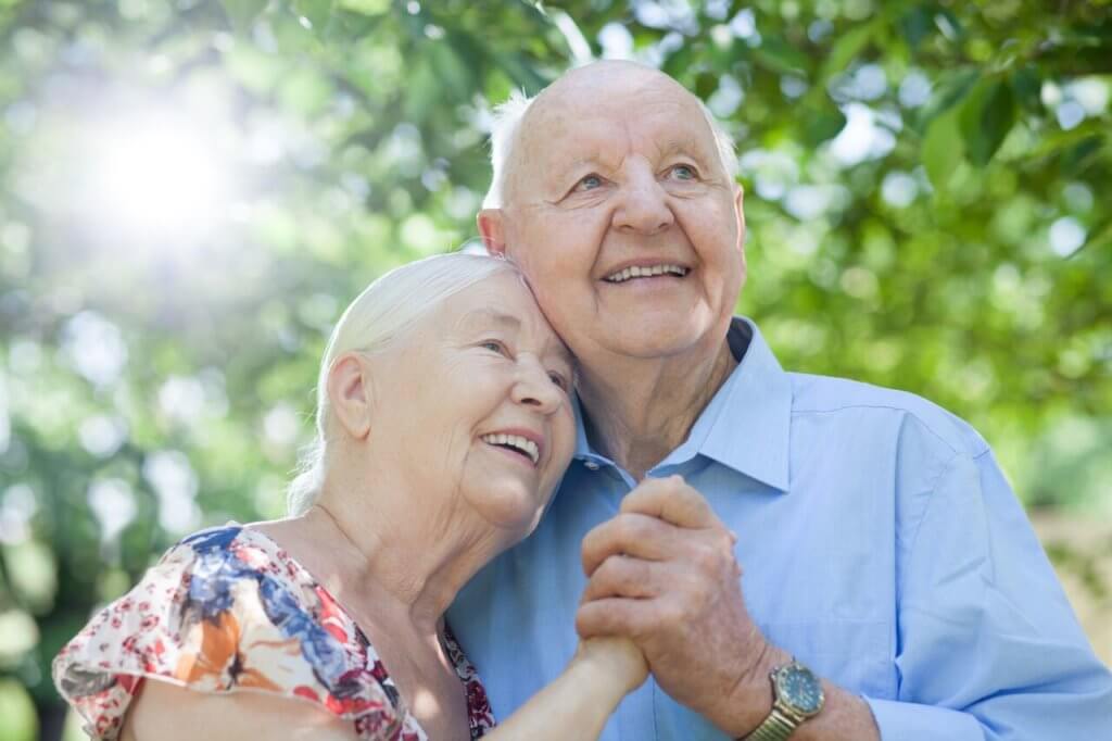 A senior couple happily embracing each other while holding hands.