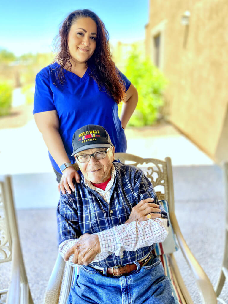 A senior sitting on a chair and a caregiver on his back.
