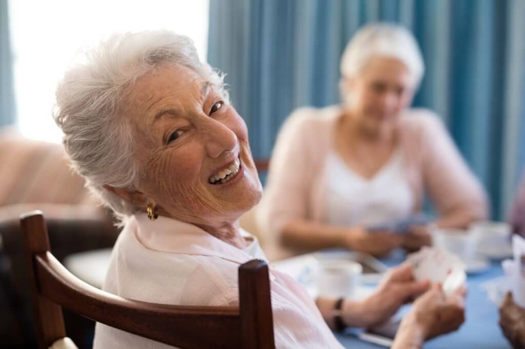 Senior happily smiling while playing cards with other seniors.