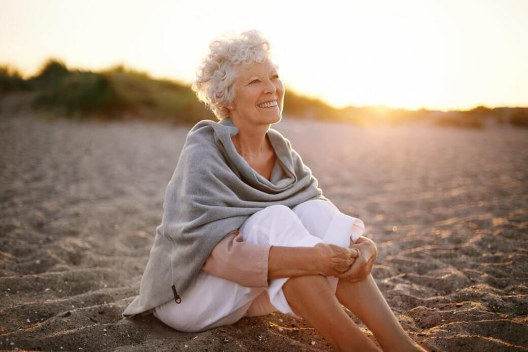 senior woman happily sitting in the sand