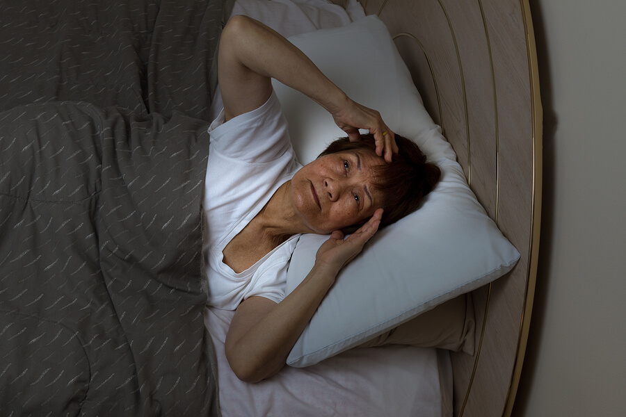 senior woman lying in hands on her head having trouble sleeping.