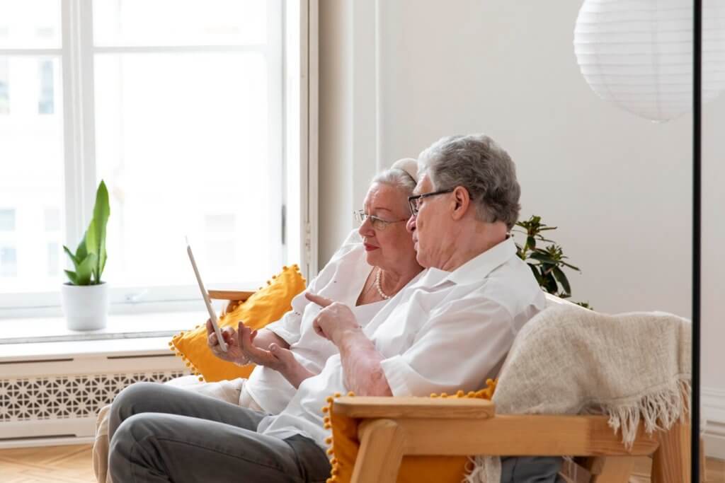 Sharing a comfortable couch, an older couple engrossed in a tablet. Embracing technology while valuing personal privacy.