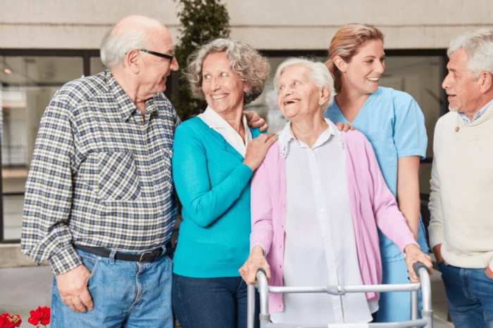 A group of individuals gathers around an elderly woman using a walker, offering support and companionship.