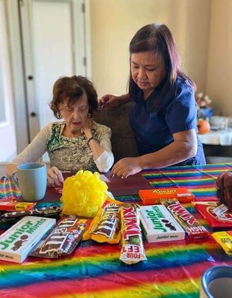 A senior and a medical staff sitting at a table with chocolates.