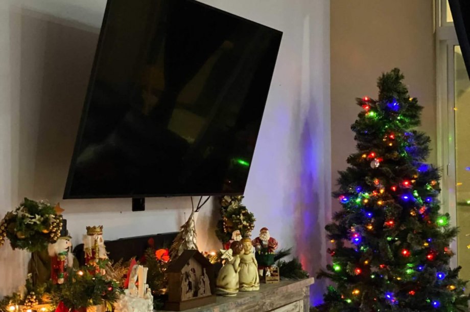 A television on a wall above a cabinet with Christmas decorations..